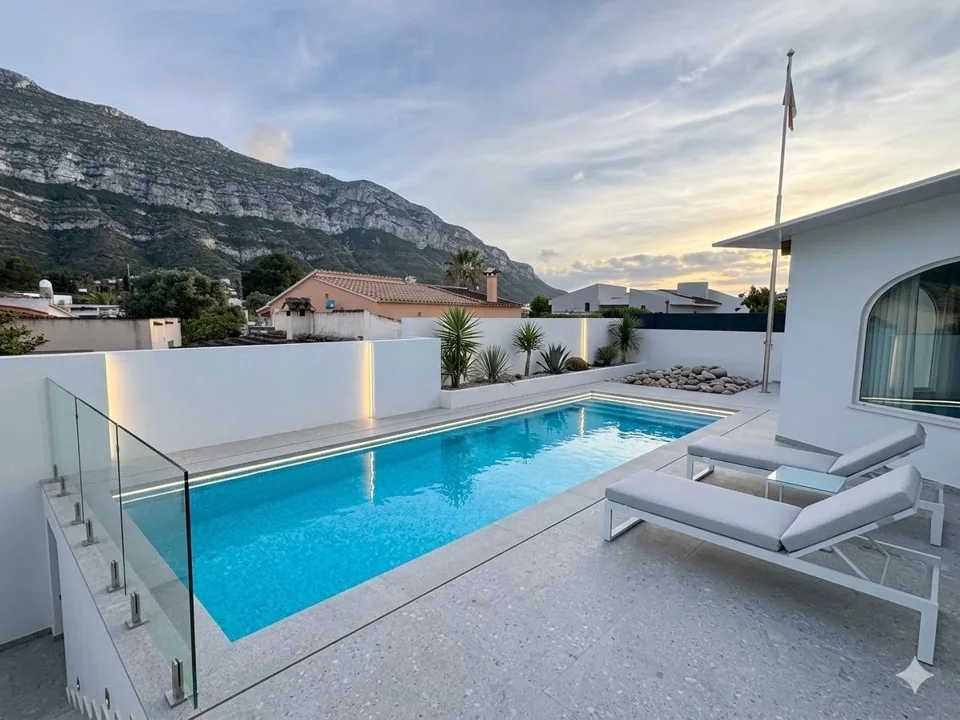 Clear swimming pool with a white terrace and mountain backdrop